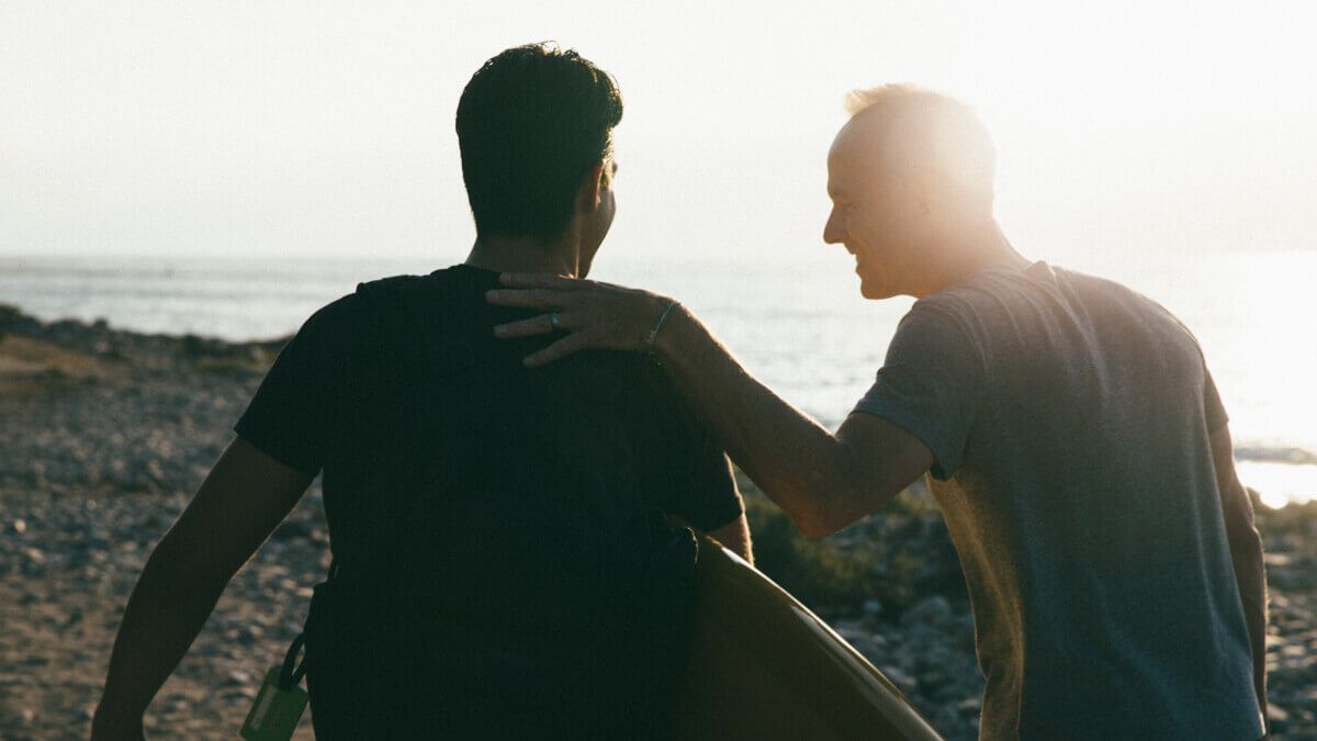 Two men with a surfboard walking towards beach